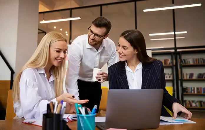 Tres personas en traje de negocios observan una computadora portátil, colaborando en un proyecto.
