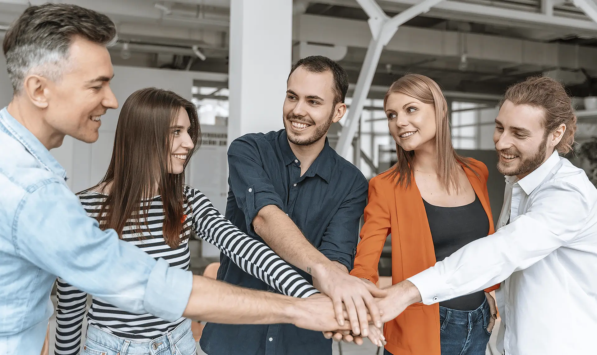 Grupo de personas de pie en una oficina, unidas de las manos, mostrando unidad y colaboración.